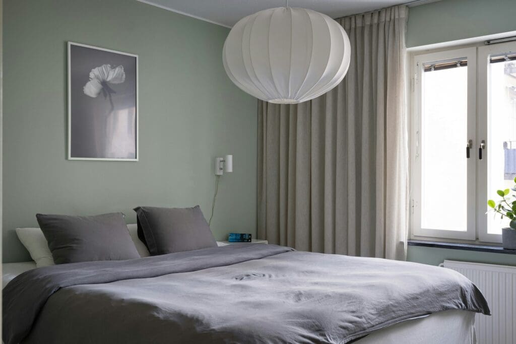 Hotel room wide angle. Bed made. Cushions arranged. Curtains open. Lamp on