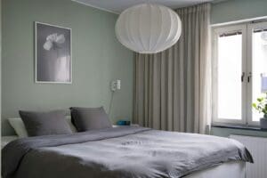 Hotel room wide angle. Bed made. Cushions arranged. Curtains open. Lamp on